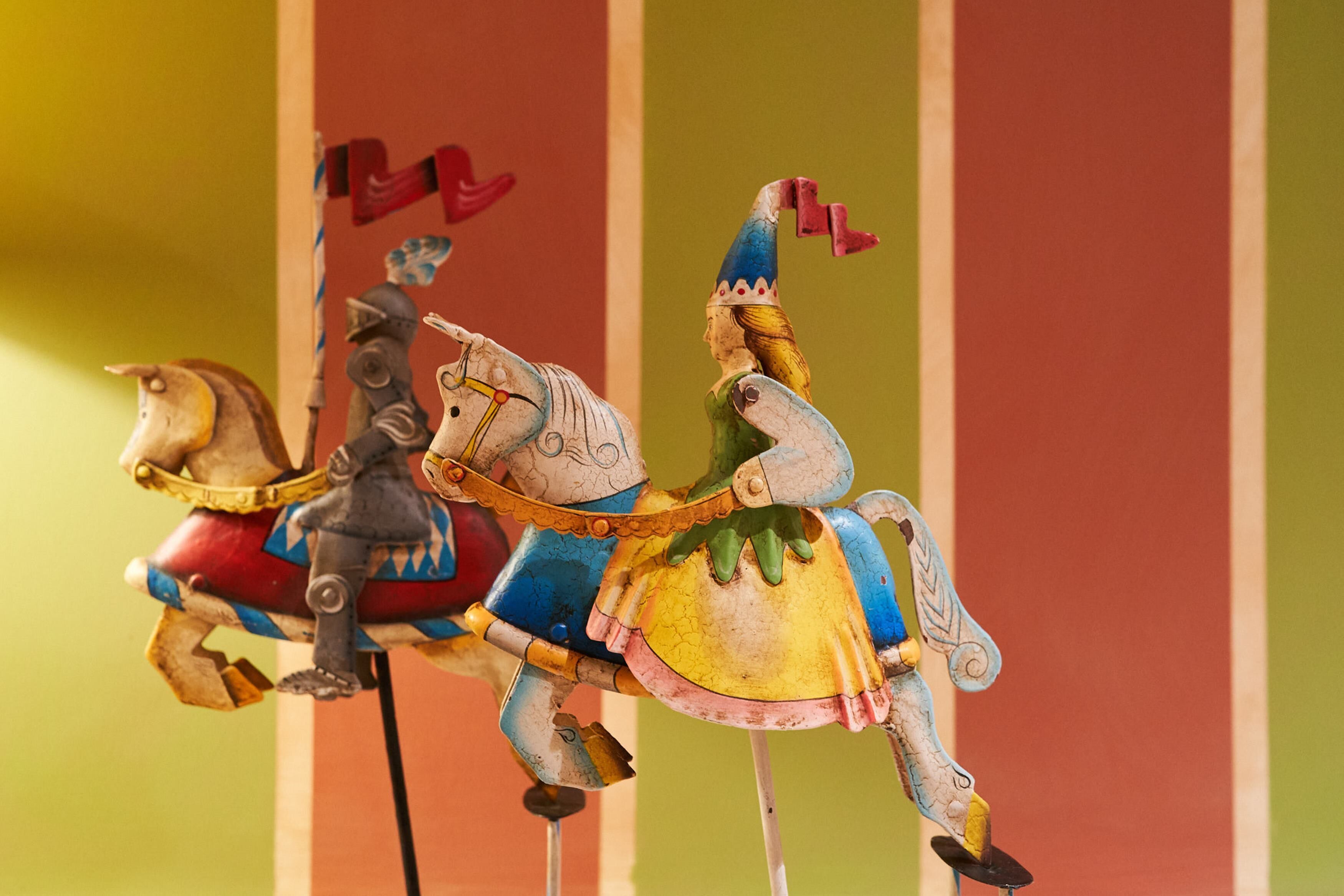 Un carrusel con caballos y jinetes coloridos, sobre un fondo a rayas.
