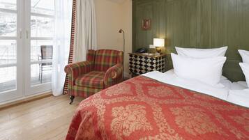A hotel room with a bed, a plaid armchair, a checkered side table, a lamp, and a view through a glass door.