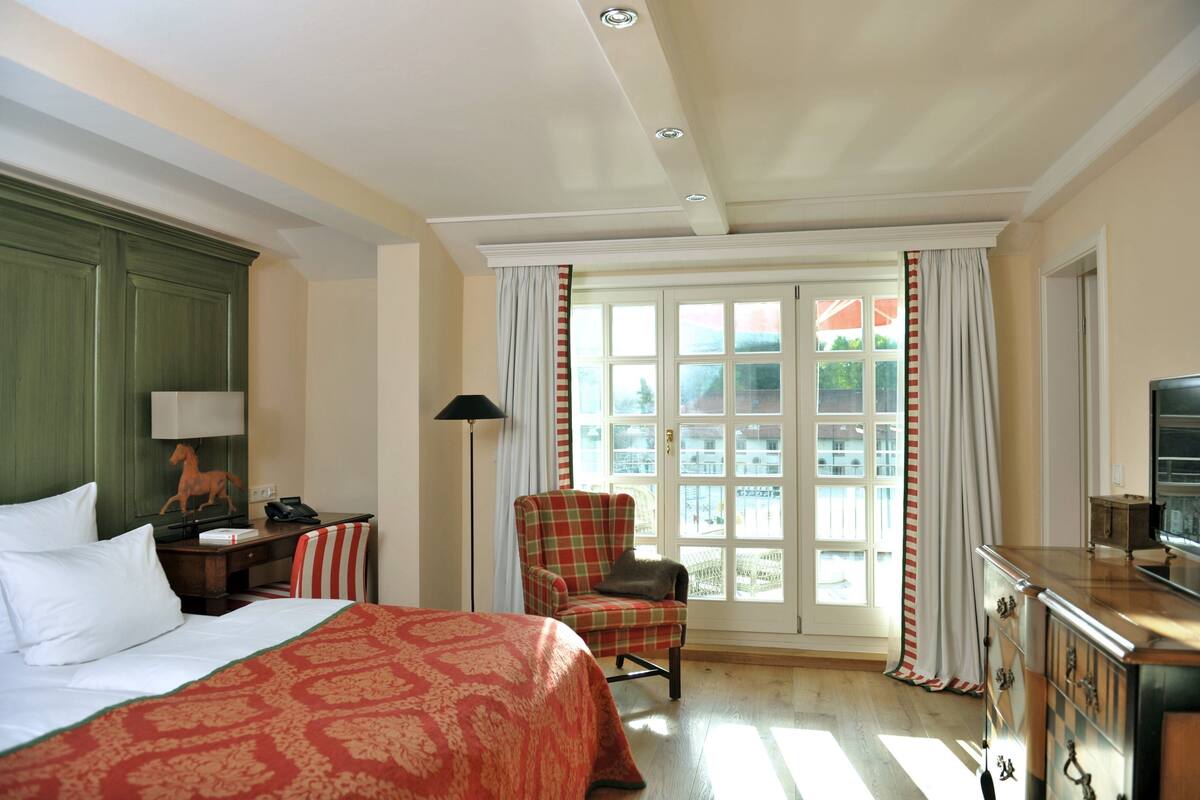 Een hotelkamer met een groot bed, een stoel, een bureau met telefoon, een televisie en een raam met gordijnen.