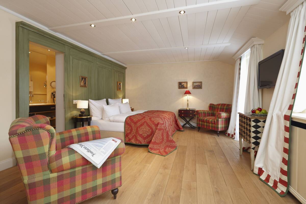 Een knus ingerichte kamer met een bed, een bank, een stoel, een klein tafeltje met fruit en een televisie.