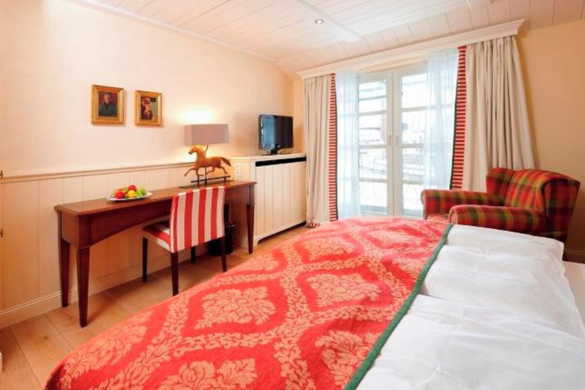 Une chambre d’hôtel avec un grand lit, un bureau avec une chaise, une télévision et une fenêtre avec des rideaux.