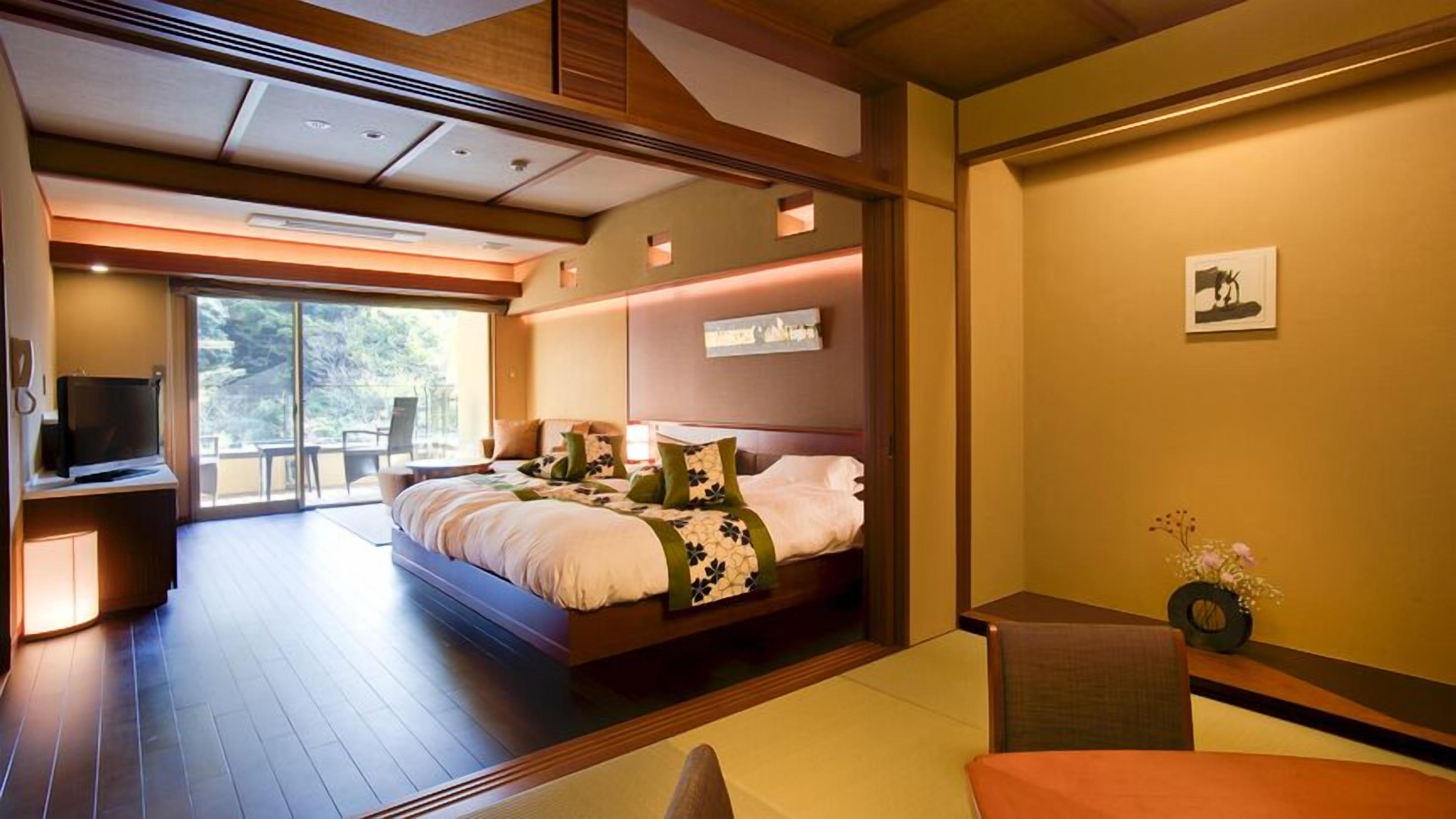 A modern hotel room with a large bed, a TV, a balcony, and a small table with a vase.