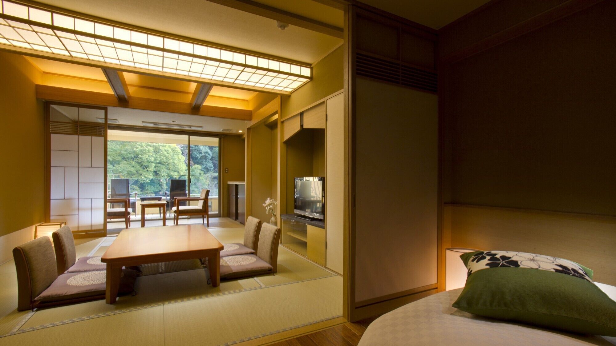 A traditional Japanese-style room with tatami flooring, a low table, chairs, a bed, and a television.