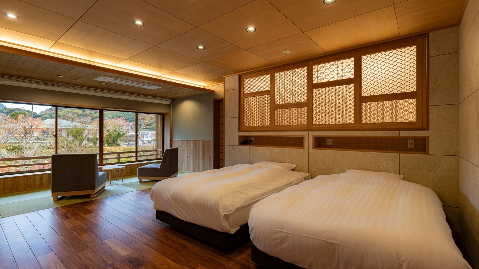 A hotel room with two beds, a view of the outside, and a traditional Japanese-style partition.