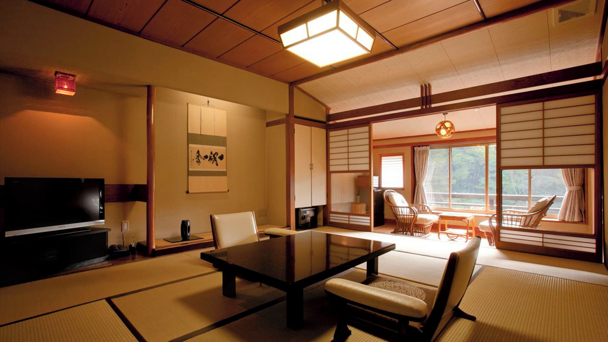 A traditional Japanese-style room with tatami flooring, a low table, chairs, a television, and sliding doors.