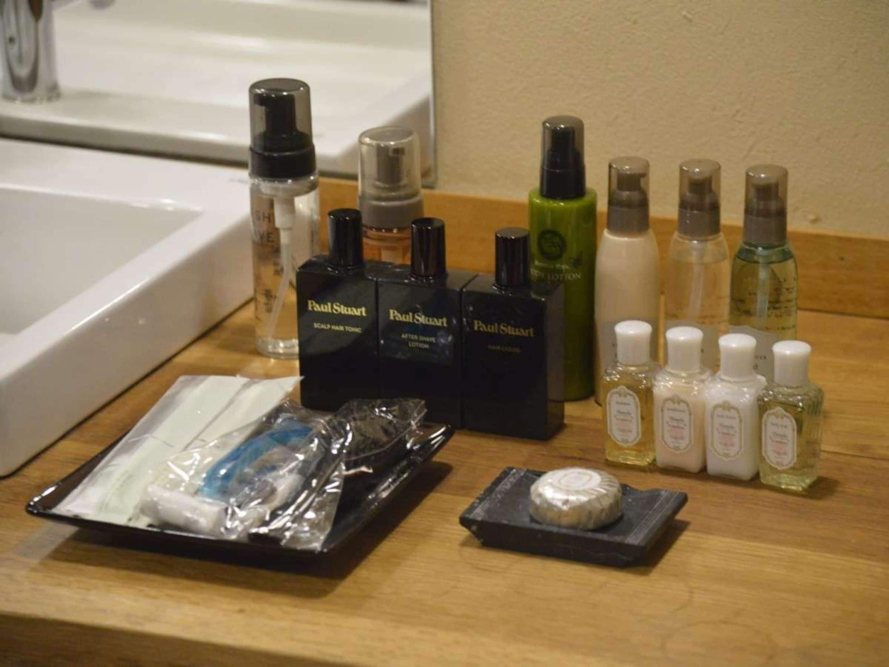 A bathroom counter with various toiletries including Paul Stuart hair care products, a razor, and a soap bar.