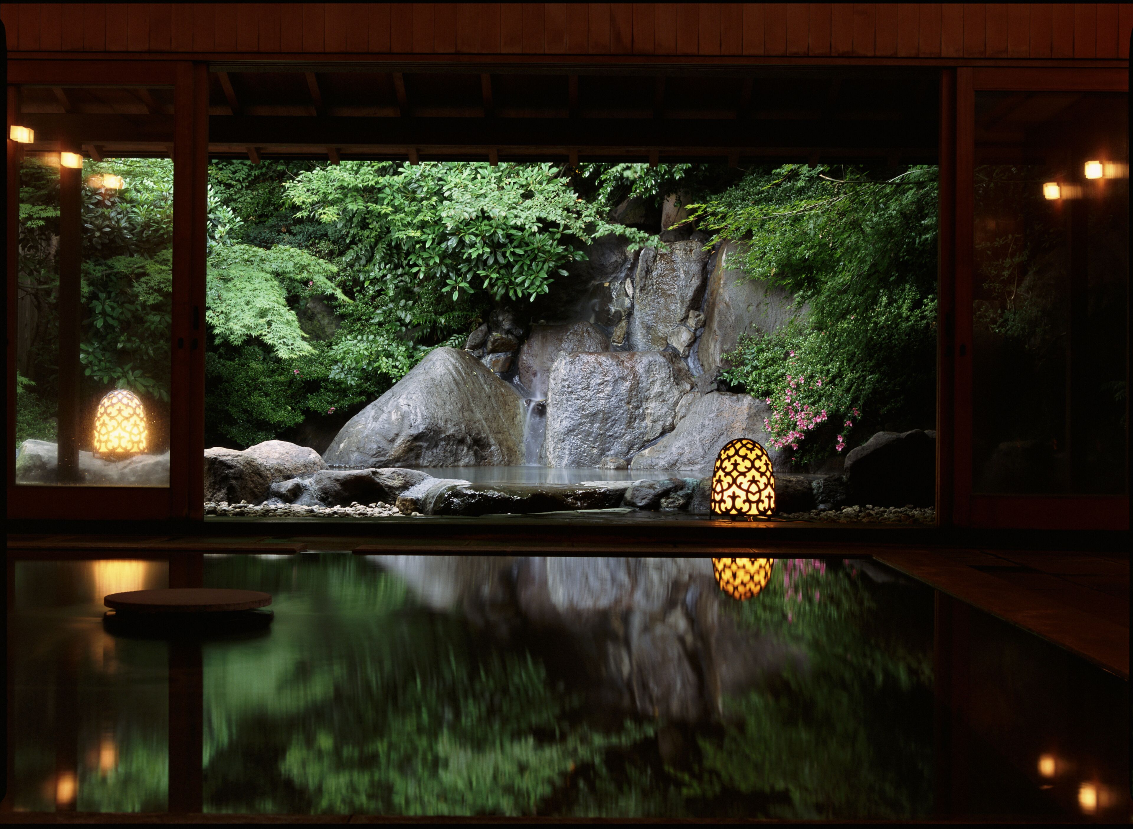 A tranquil indoor garden with a water feature, stone rocks, and lush greenery.