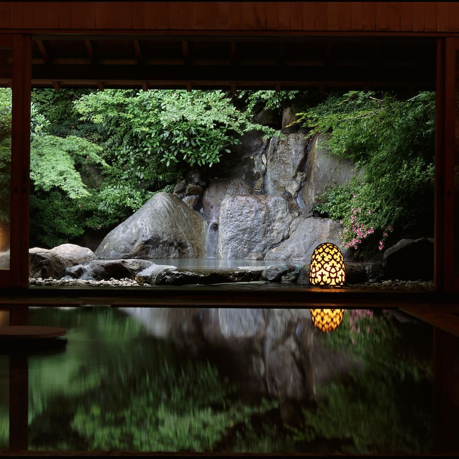 A tranquil indoor garden with a water feature, stone rocks, and lush greenery.