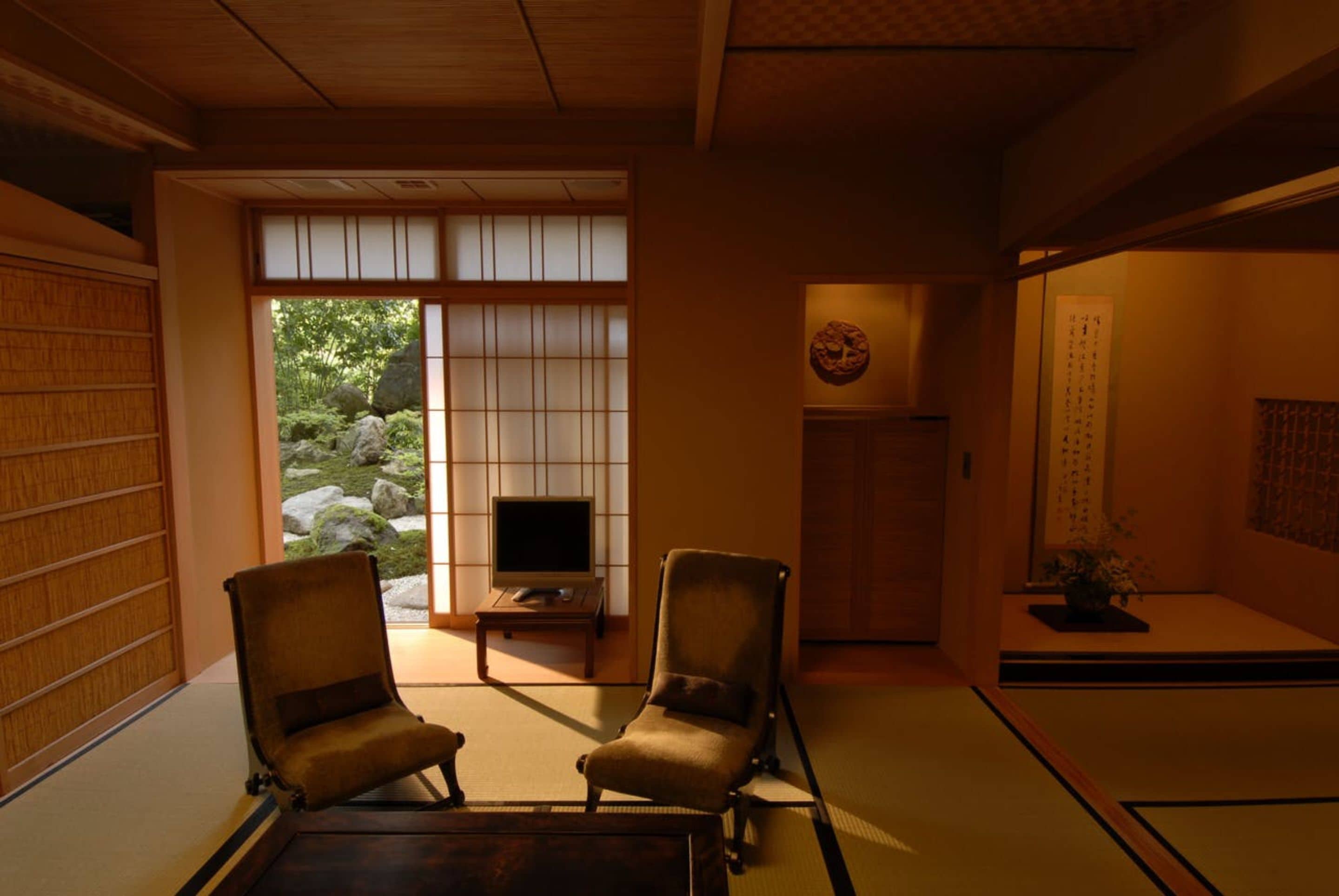 A traditional Japanese room with tatami flooring, two tatami mats, a television on a low table, and a sliding door leading to a garden.