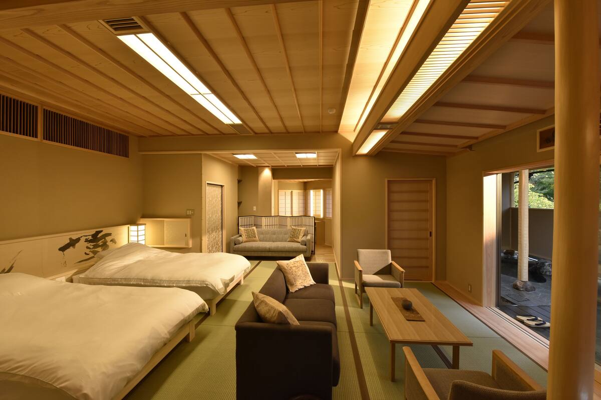 Una habitación tradicional japonesa con suelo de tatami, techo de madera bajo y puertas correderas que dan a un espacio exterior.