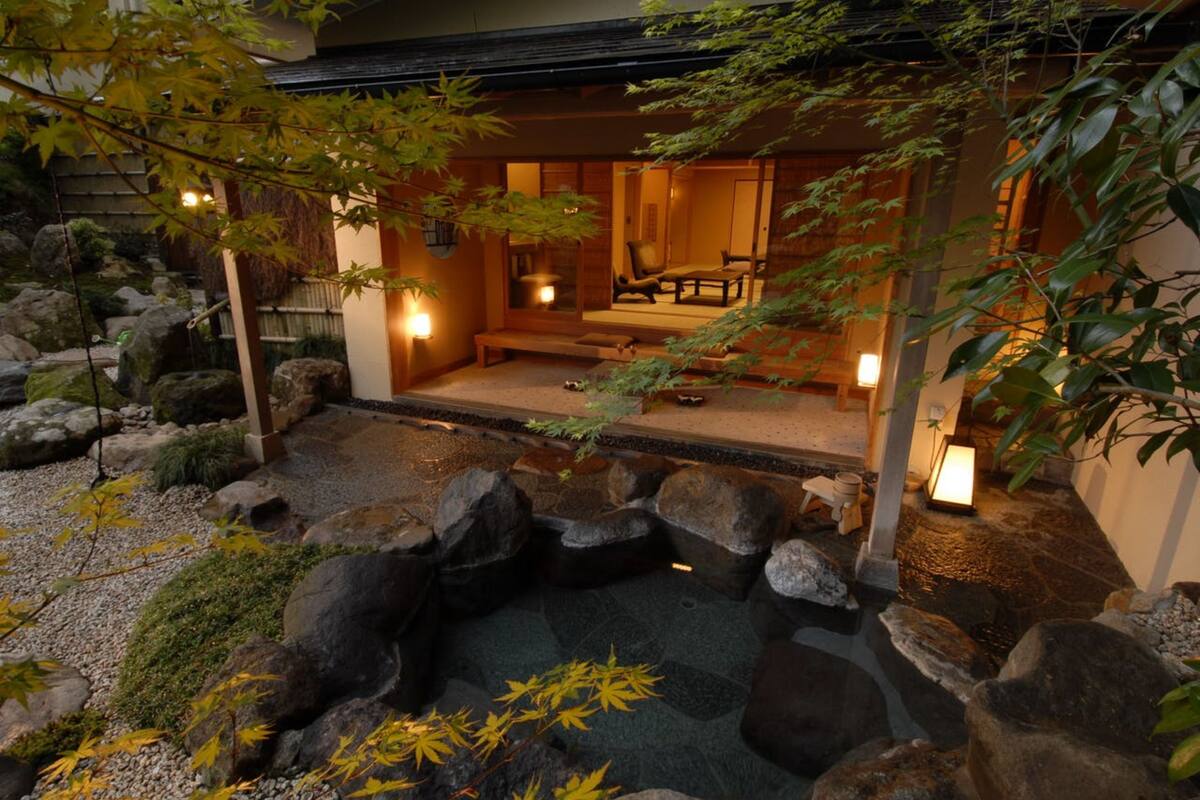 Un jardín japonés tradicional con un estanque de peces koi, rocas y una estructura de madera con asientos.