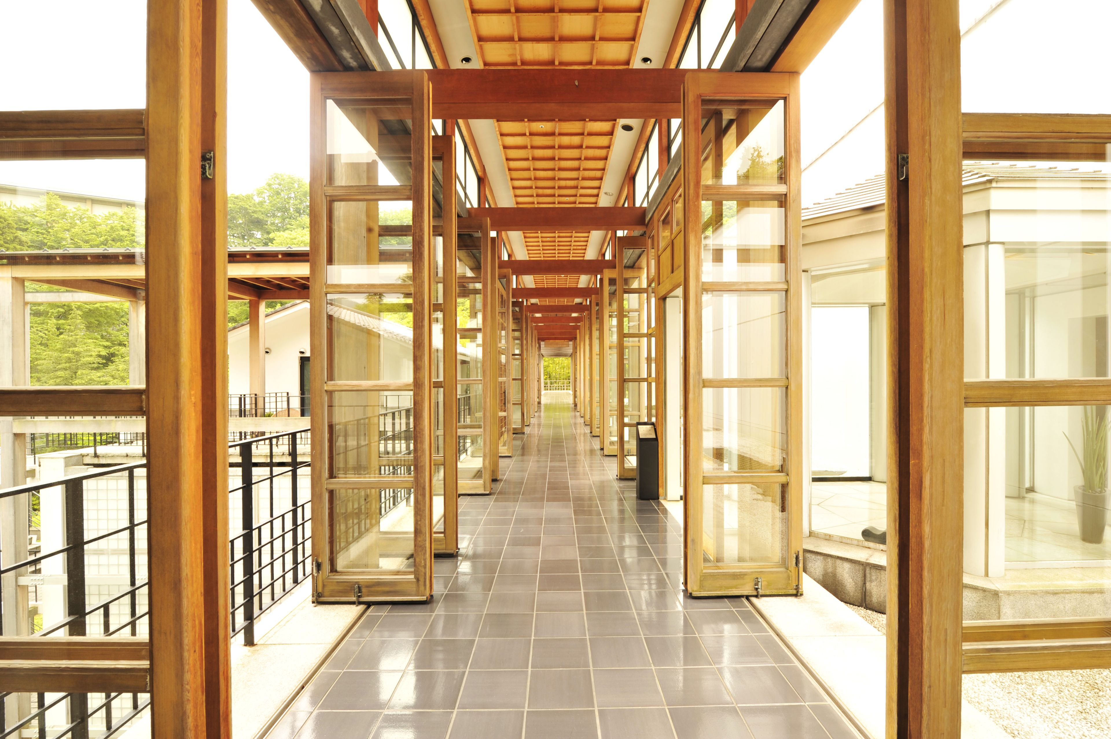 A corridor with glass doors and windows, wooden beams, and a tiled floor.