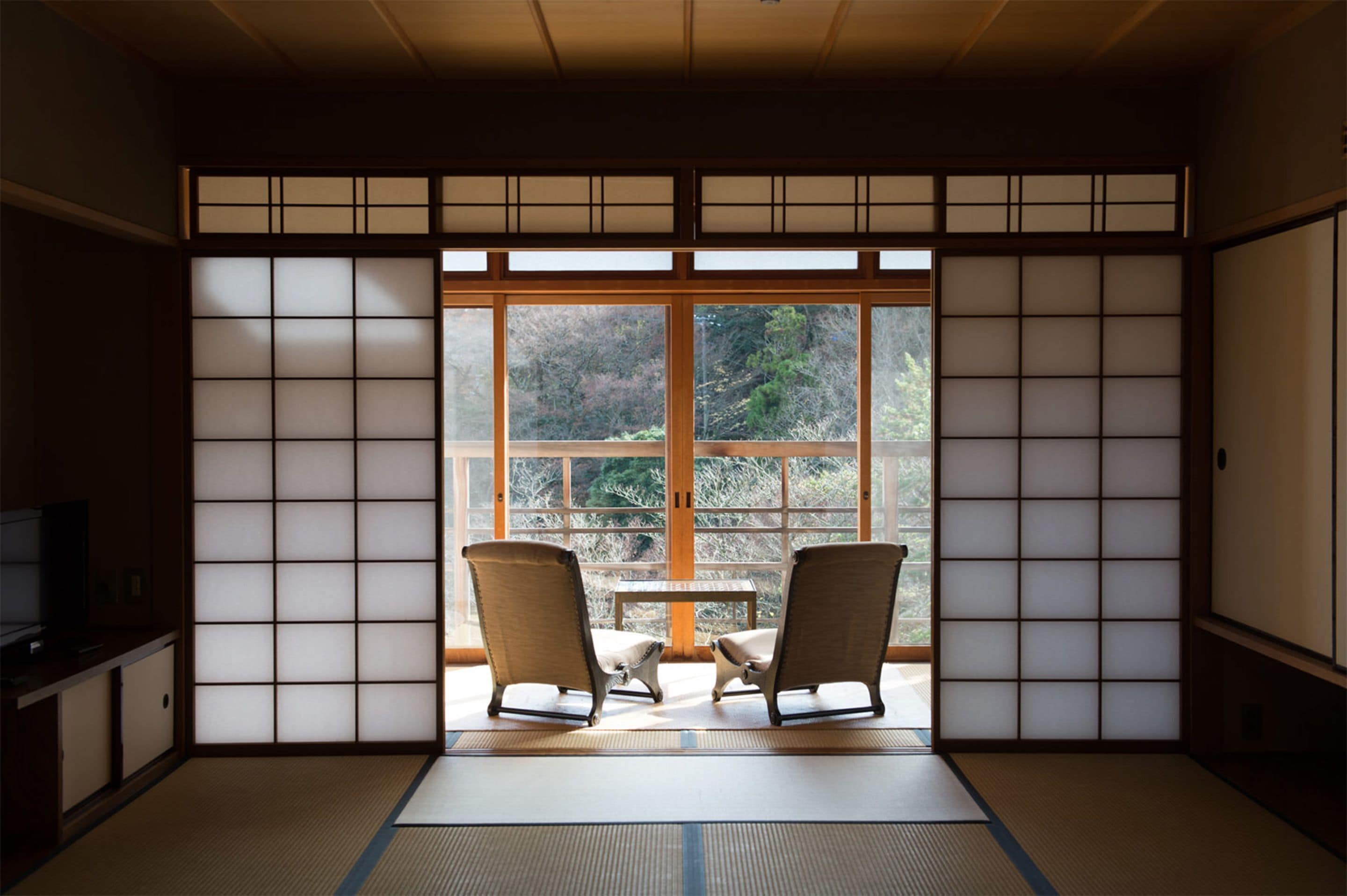 Um quarto japonês tradicional com tatame, portas deslizantes shoji e vista para um jardim.
