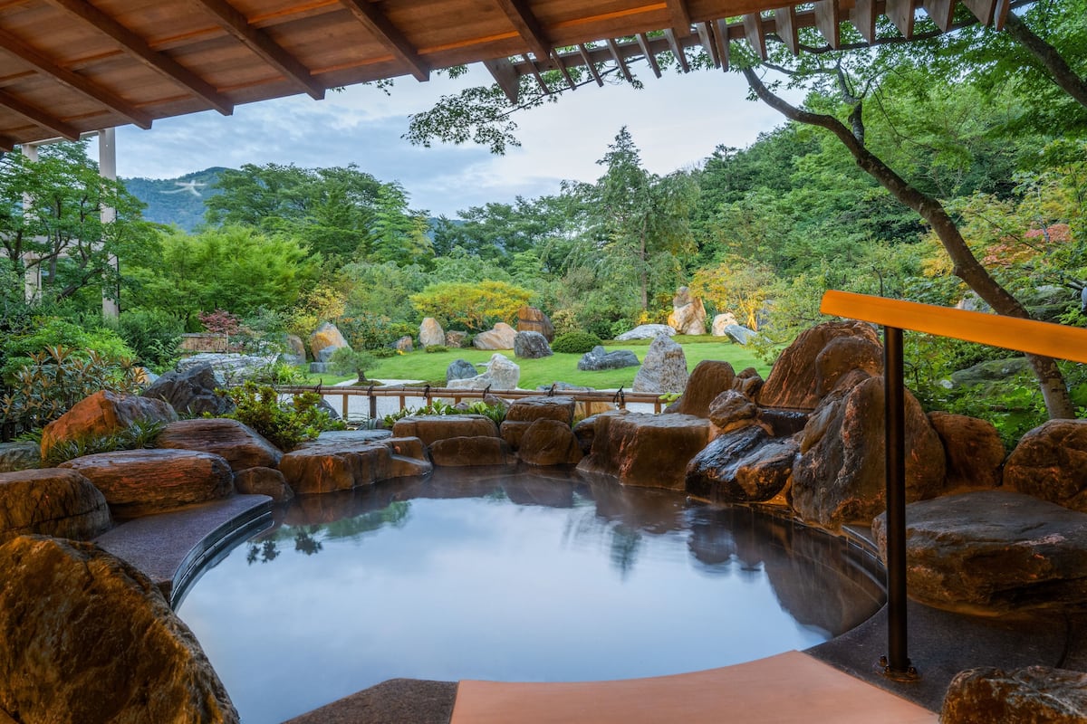 Un jardín tranquilo con aguas termales, rocas grandes y un puente de madera.