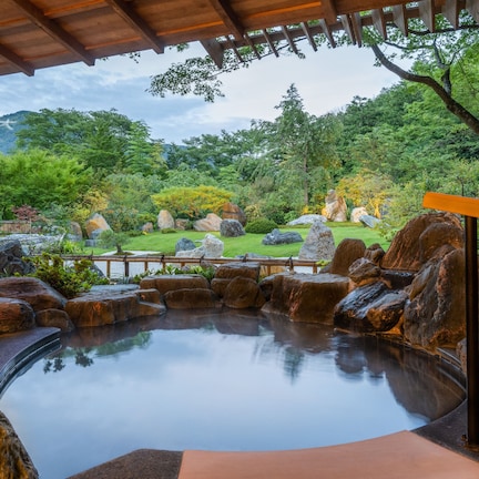 A tranquil garden with a hot spring, large rocks, and a wooden bridge.
