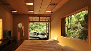 Un dormitorio con una cama grande, un televisor sobre un mueble, una ventana con vistas a zonas verdes y un techo de madera.