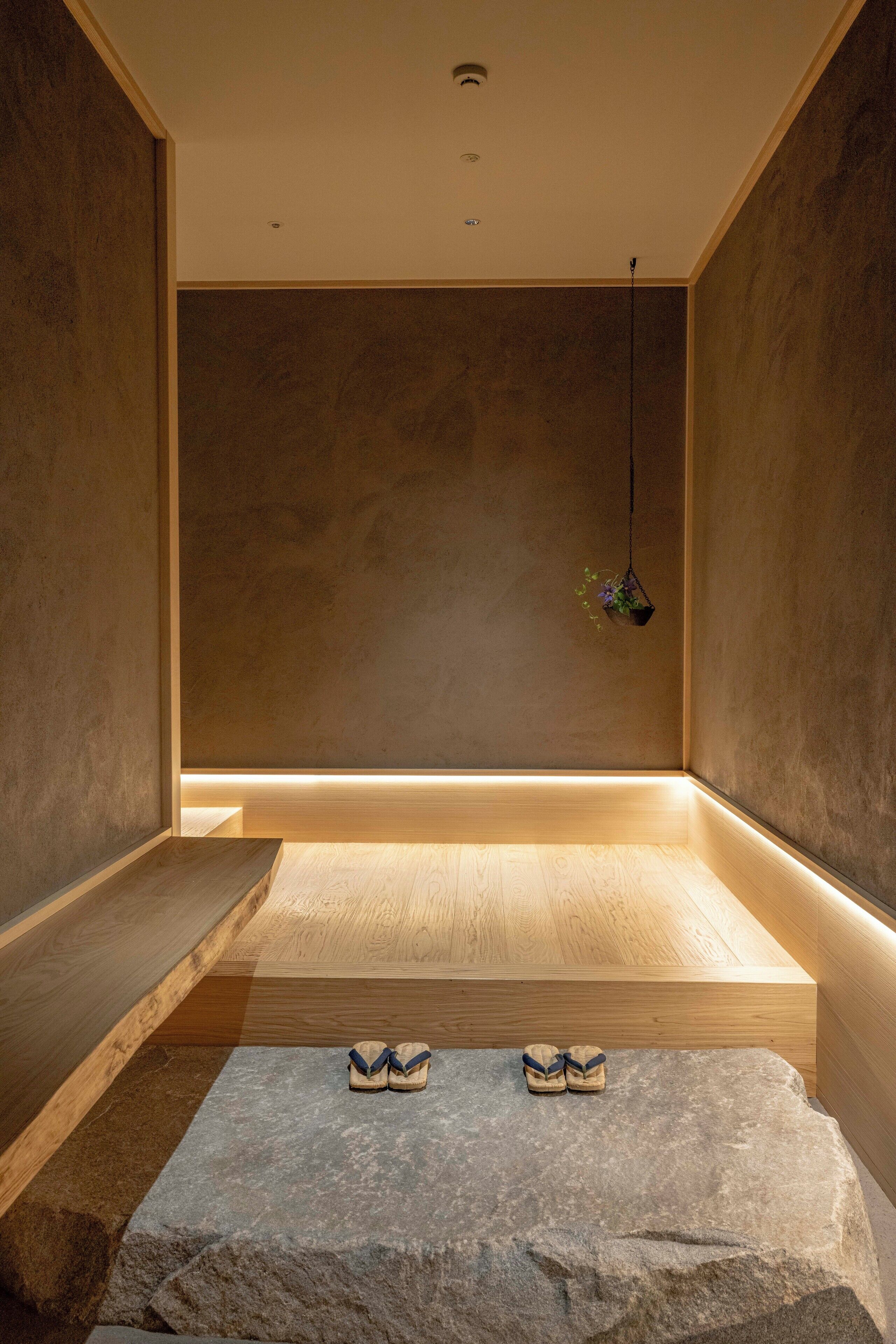 A minimalist room with a wooden bench, a stone platform, and a hanging plant.