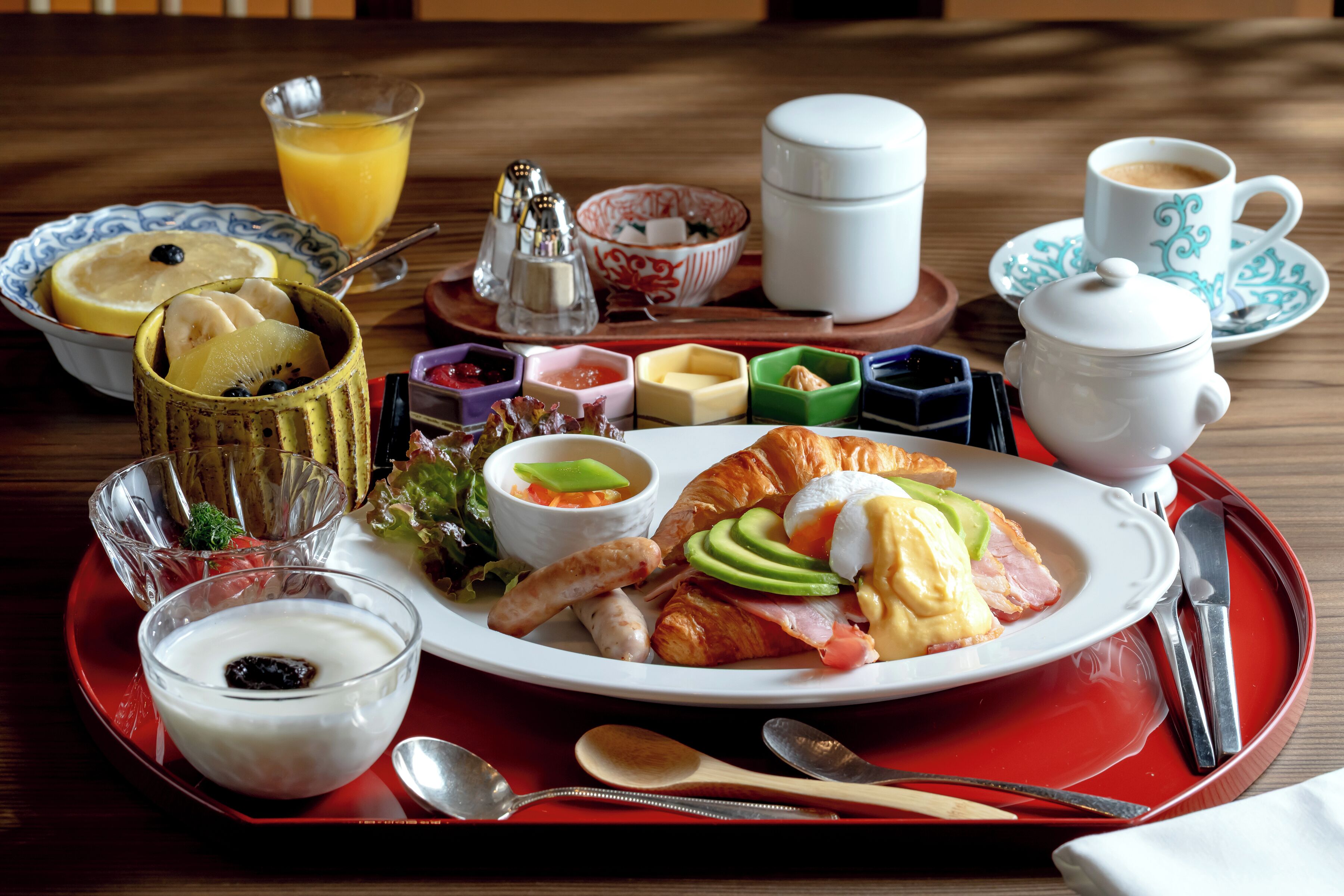 Bandeja de desayuno con un croissant, jamón, huevos y un vaso de zumo de naranja.