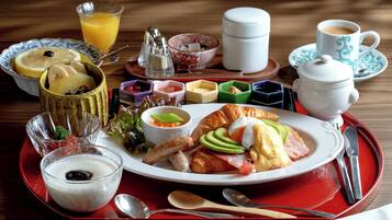 Bandeja de desayuno con un croissant, jamón, huevos y un vaso de zumo de naranja.