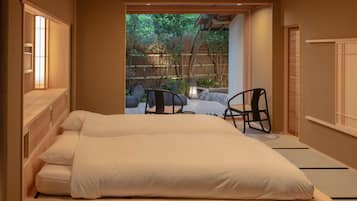 A traditional Japanese-style room with tatami flooring, a low wooden bed, and a view of a bamboo garden.