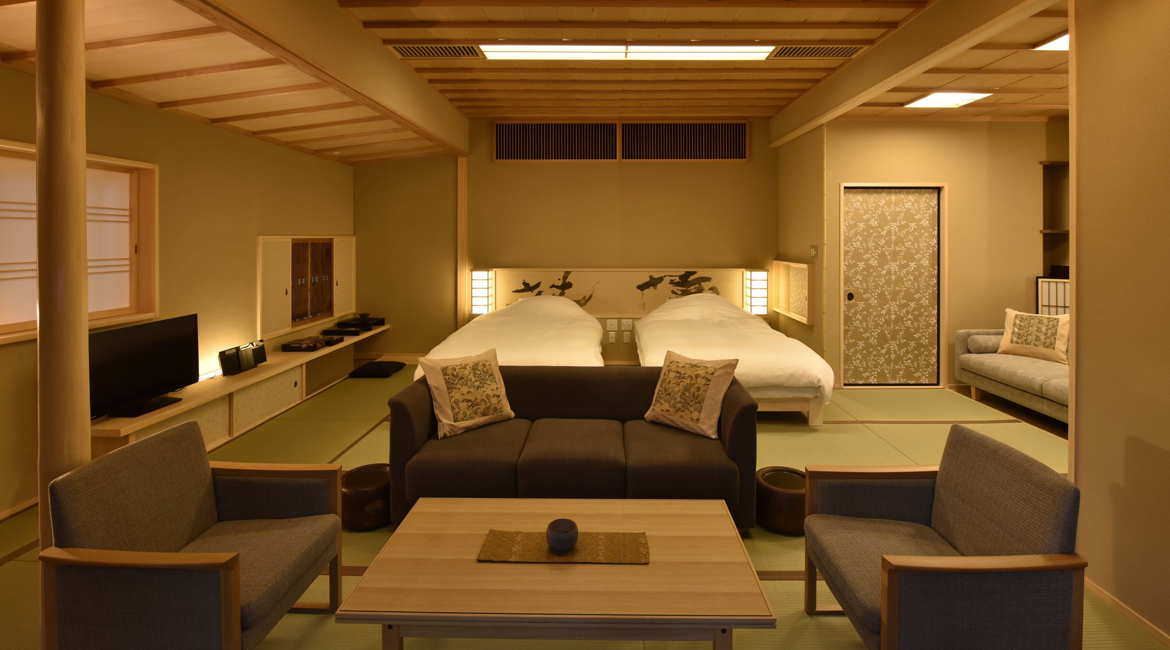 A hotel room with a sofa, two beds, a TV, a table, and a decorative wall.