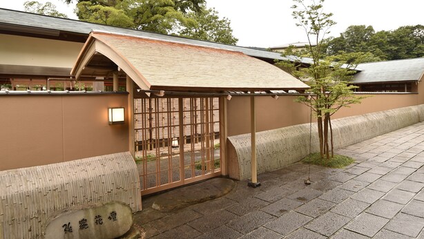 Un edificio japonés tradicional con tejado de tejas, una puerta de madera y una piedra con caracteres japoneses.