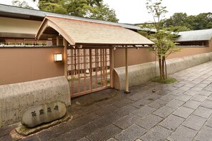 Un bâtiment japonais traditionnel, avec un toit recouvert de tuiles, une porte en bois et une pierre portant des caractères japonais.