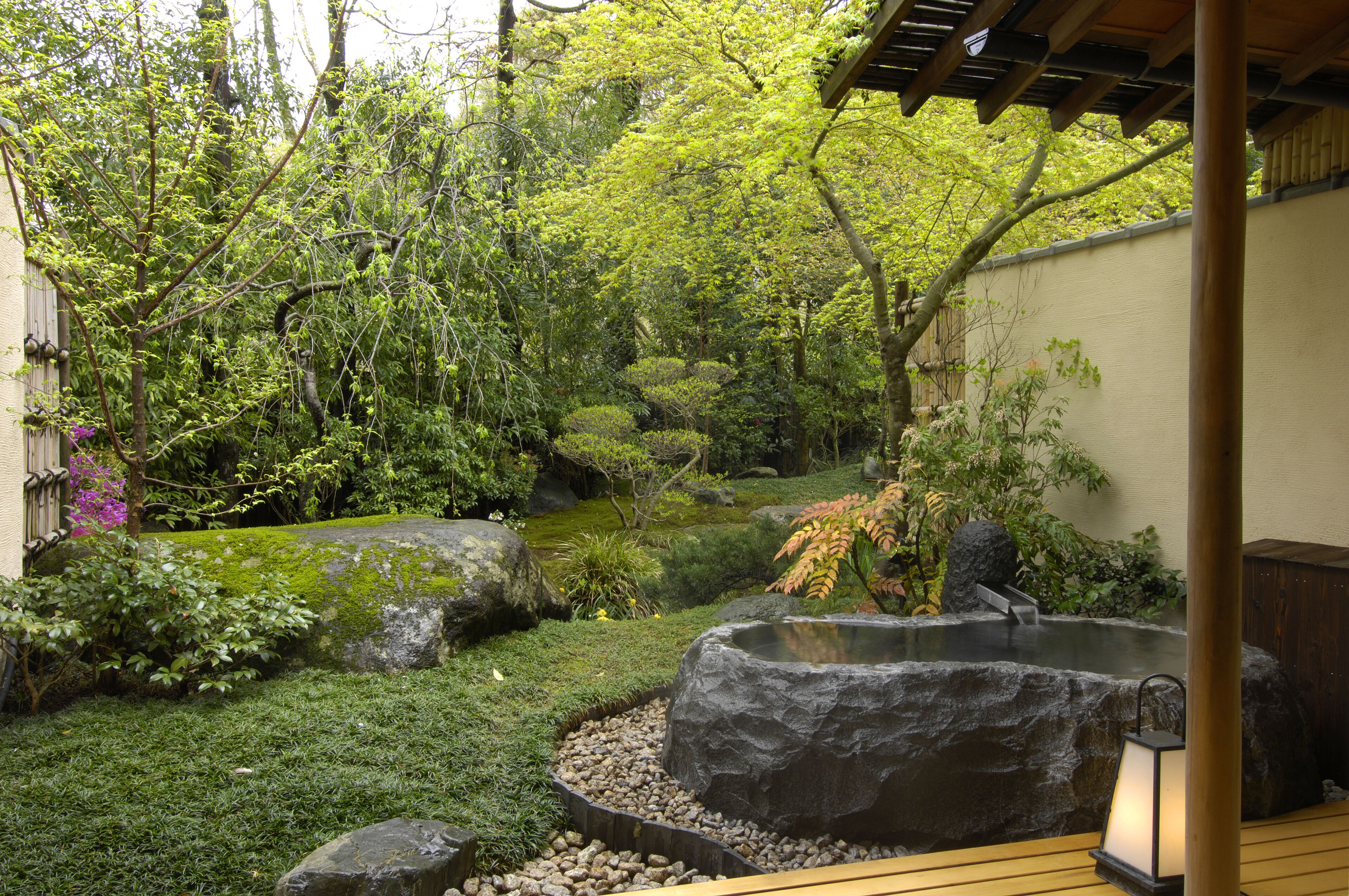 Un jardín tranquilo con un estanque de peces koi, rocas grandes y abundante vegetación.