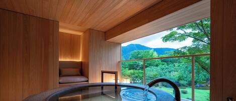 Un spa moderno con un jacuzzi de piedra, paredes de madera y un amplio ventanal con vistas a un exuberante jardín.