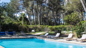 A swimming pool with lounge chairs and tall trees in the background.
