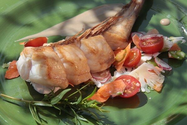 Un plato con pescado, tomates, rábanos y hierbas.
