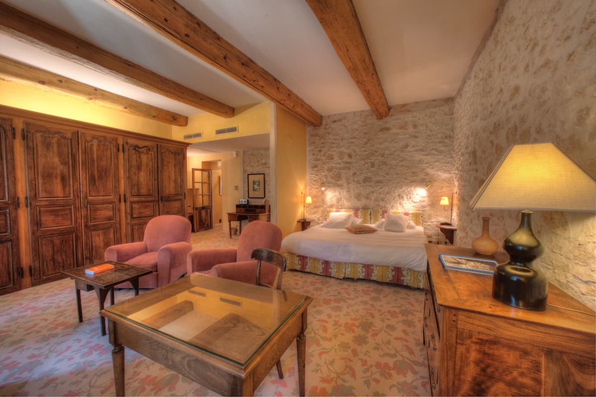 A room with a bed, two chairs, a table, and a lamp.