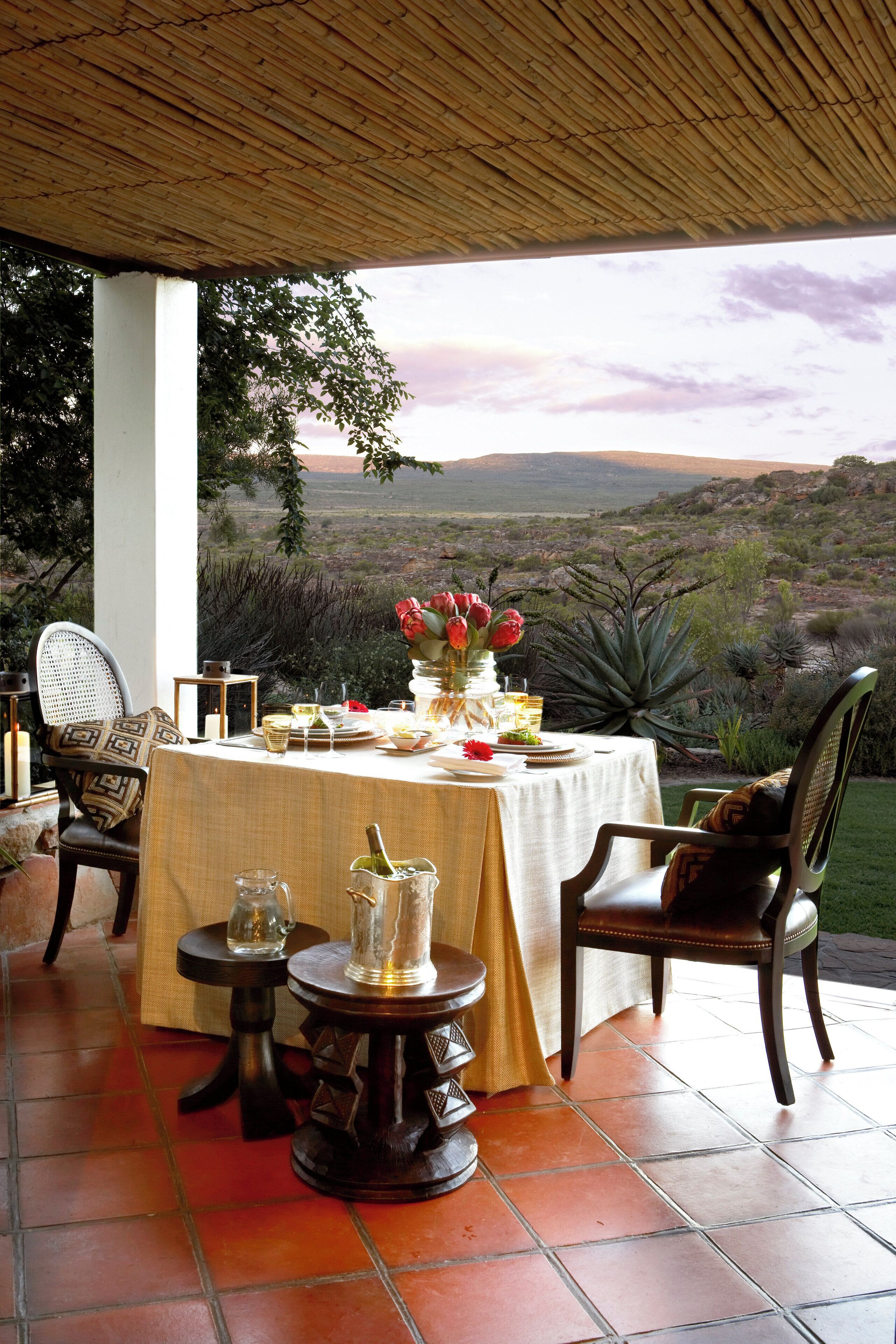 Un área de comedor al aire libre con una mesa dispuesta para dos personas, rodeada de sillas y vistas al paisaje.