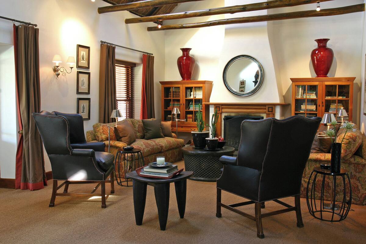 Una sala de estar acogedora con sillones de cuero, un sofá y una mesa de centro con libros. Hay estanterías, una chimenea y un espejo grande en la pared.