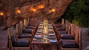 Une longue table à manger, dressée pour un repas, avec des chaises de chaque côté, placée devant une grande formation rocheuse.
