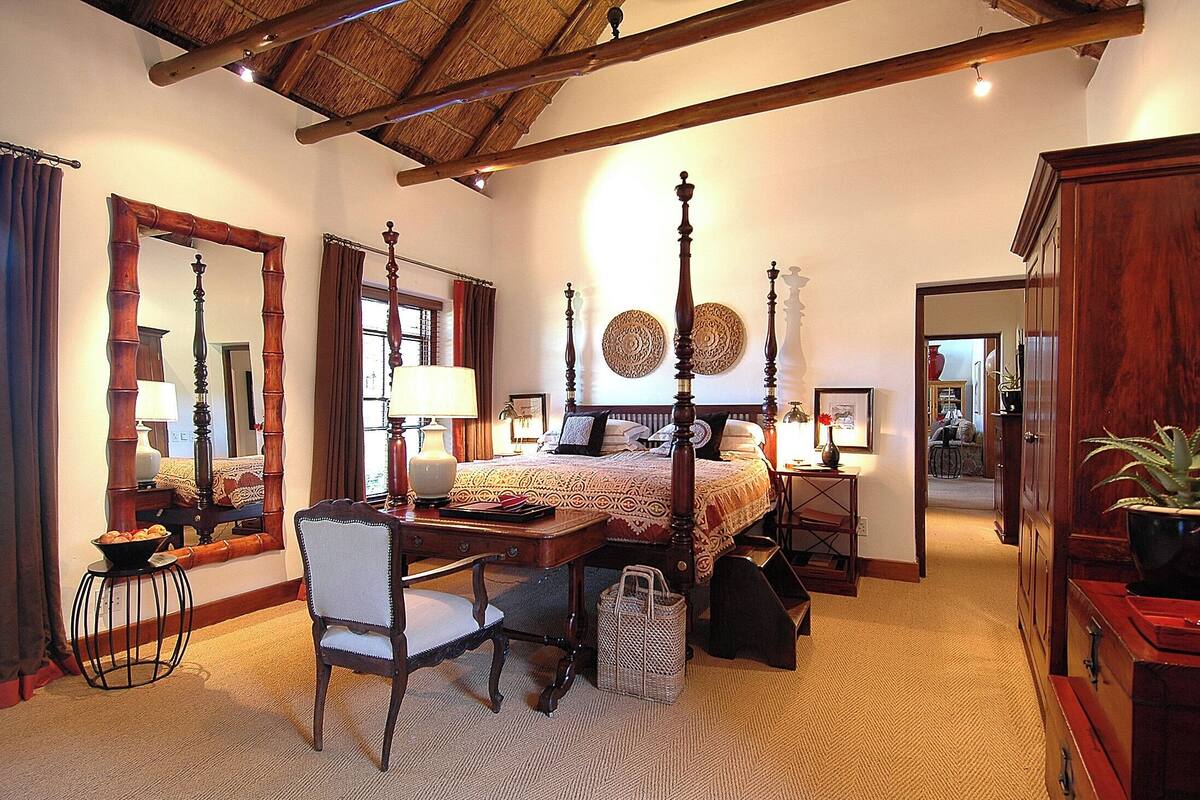 Une chambre à coucher de style traditionnel, avec un lit à baldaquin, un bureau avec une chaise et un grand miroir.