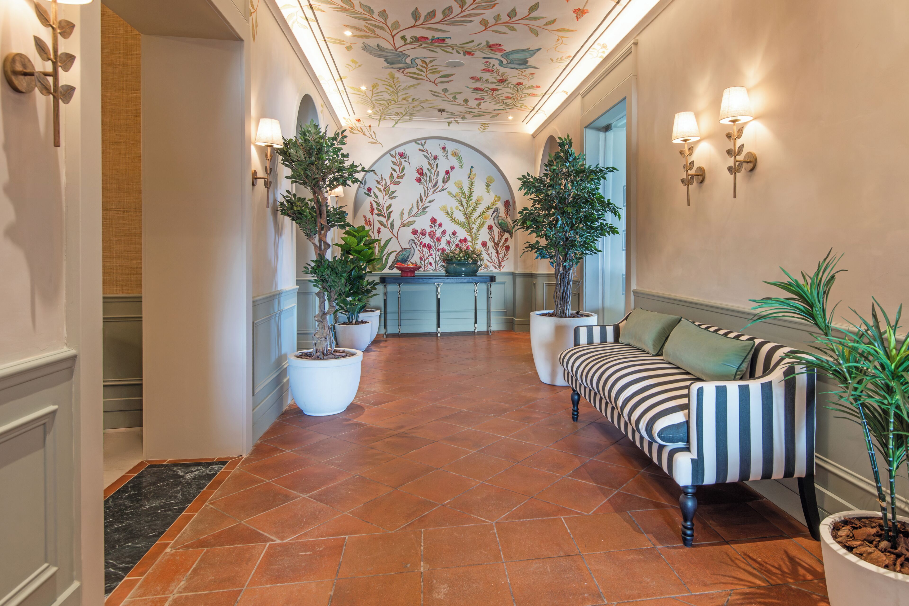 A hallway with a tiled floor, a striped sofa, potted plants, and a decorative ceiling.
