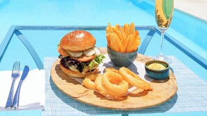 A poolside dining setup with a burger, fries, onion rings, and a glass of champagne.