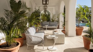 A sunlit patio with a wicker sofa, a small table, and potted plants.