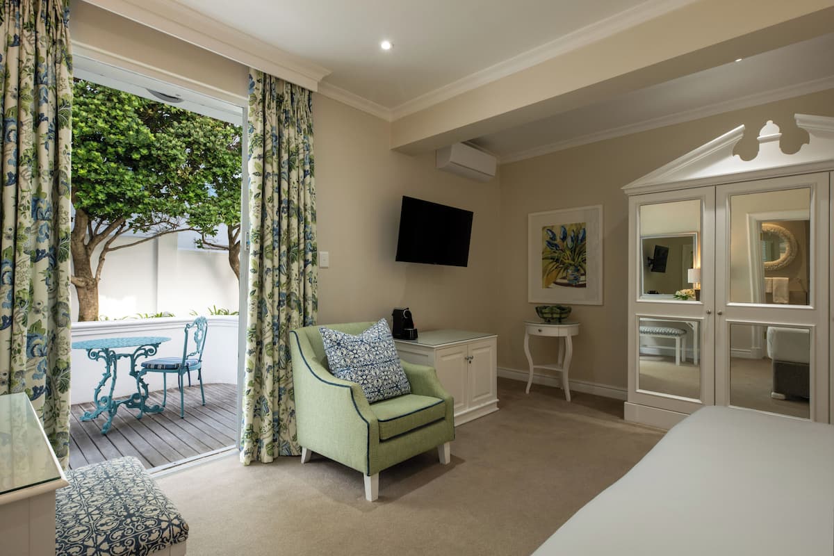 A bedroom with a green armchair, a bedside table, a TV, a wardrobe, and a balcony with a table and chairs.
