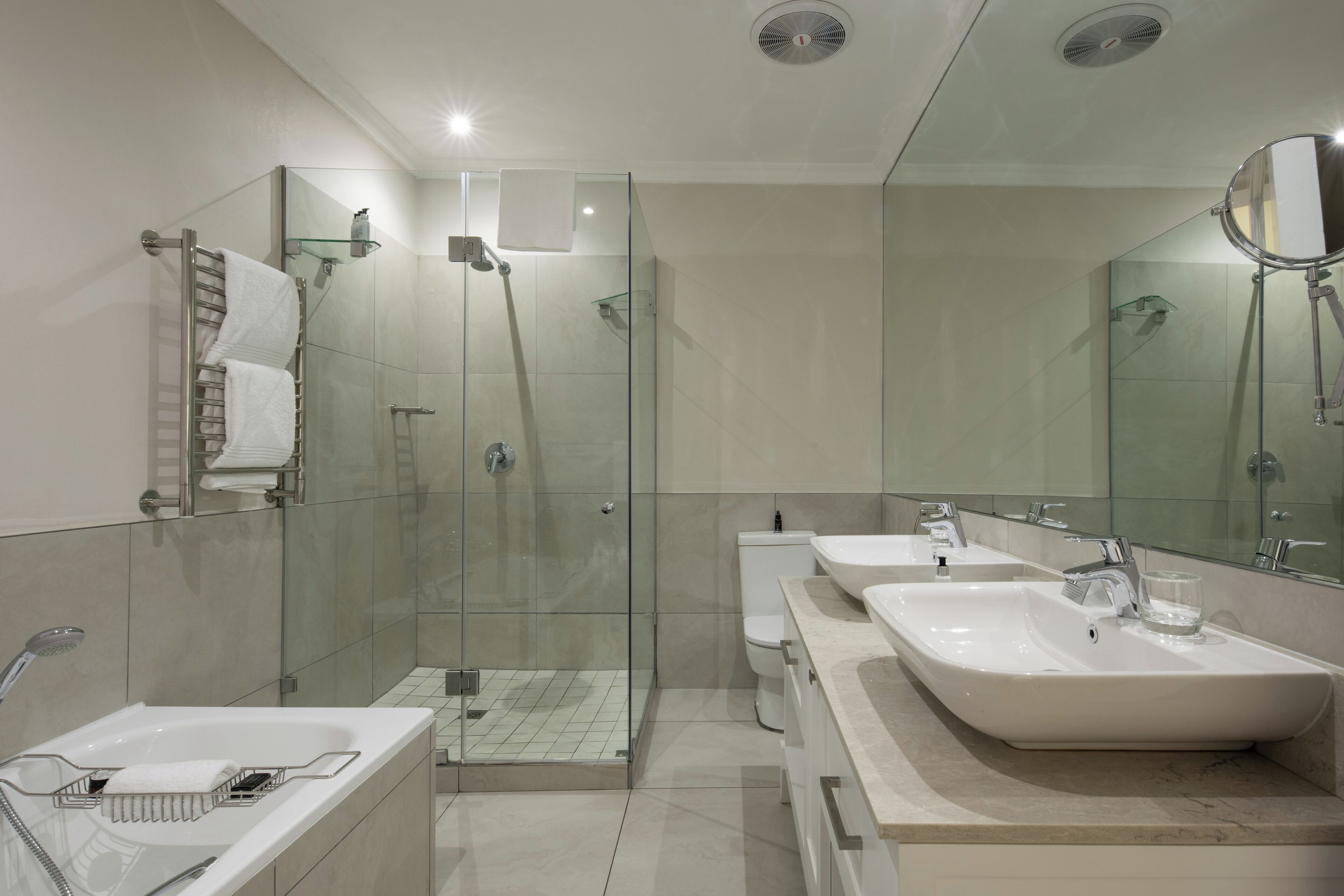 Un baño moderno con ducha de vidrio, dos lavamanos y un espejo grande.