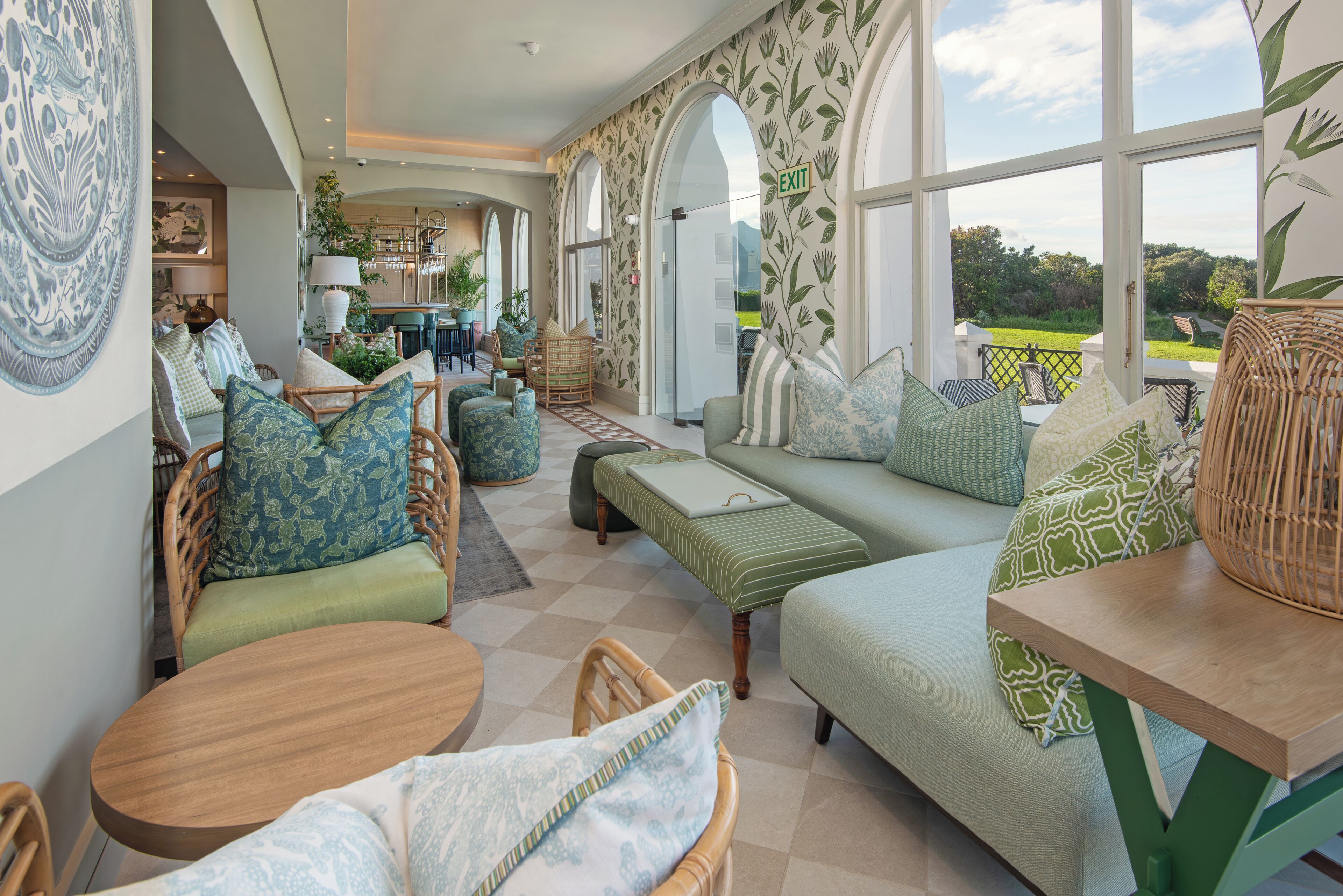 A spacious room with a large window, a sofa, a round table, and a dining area in the background.