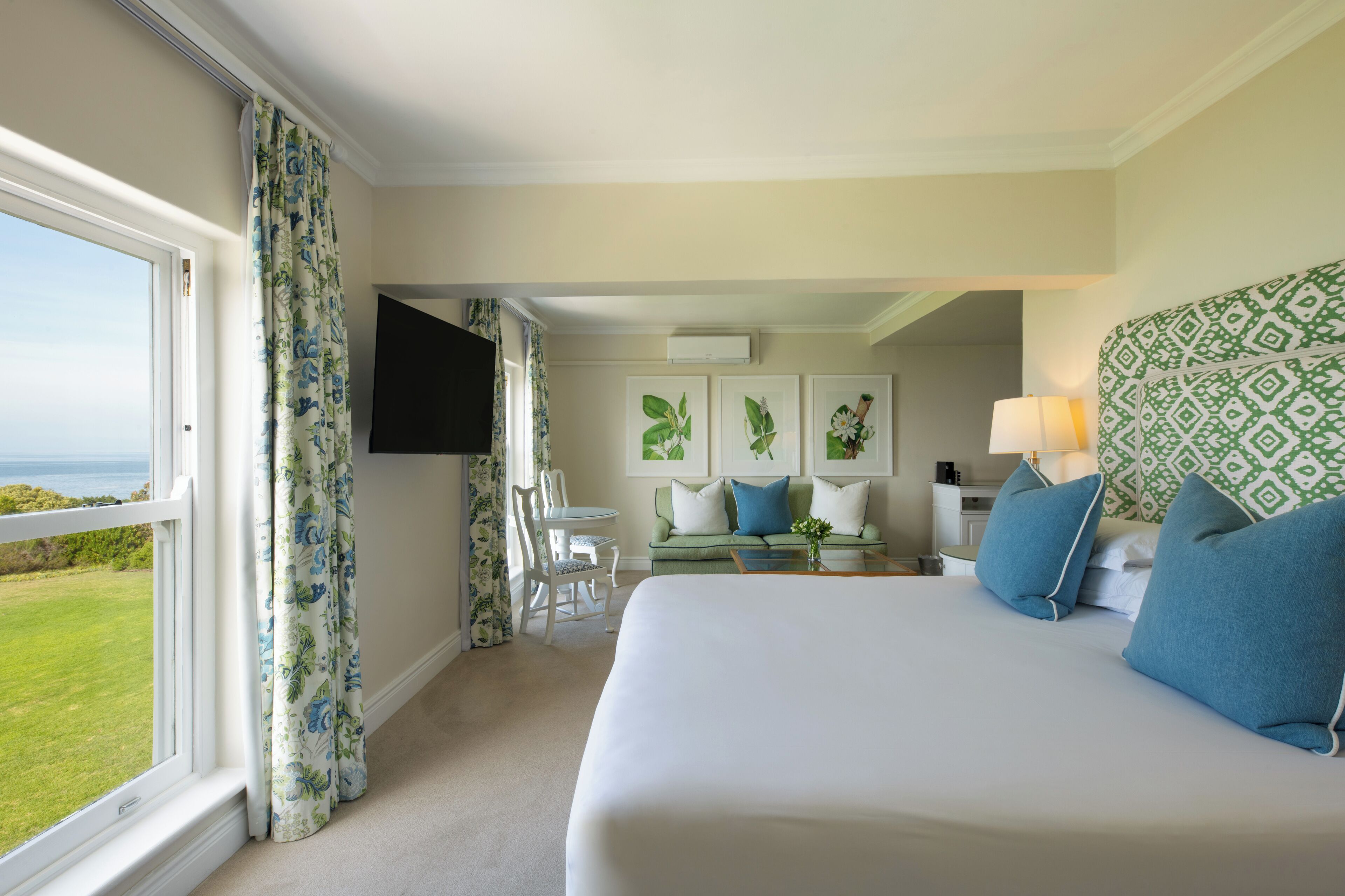 A hotel room with a large bed, a sofa, a TV, and a view of the outdoors.