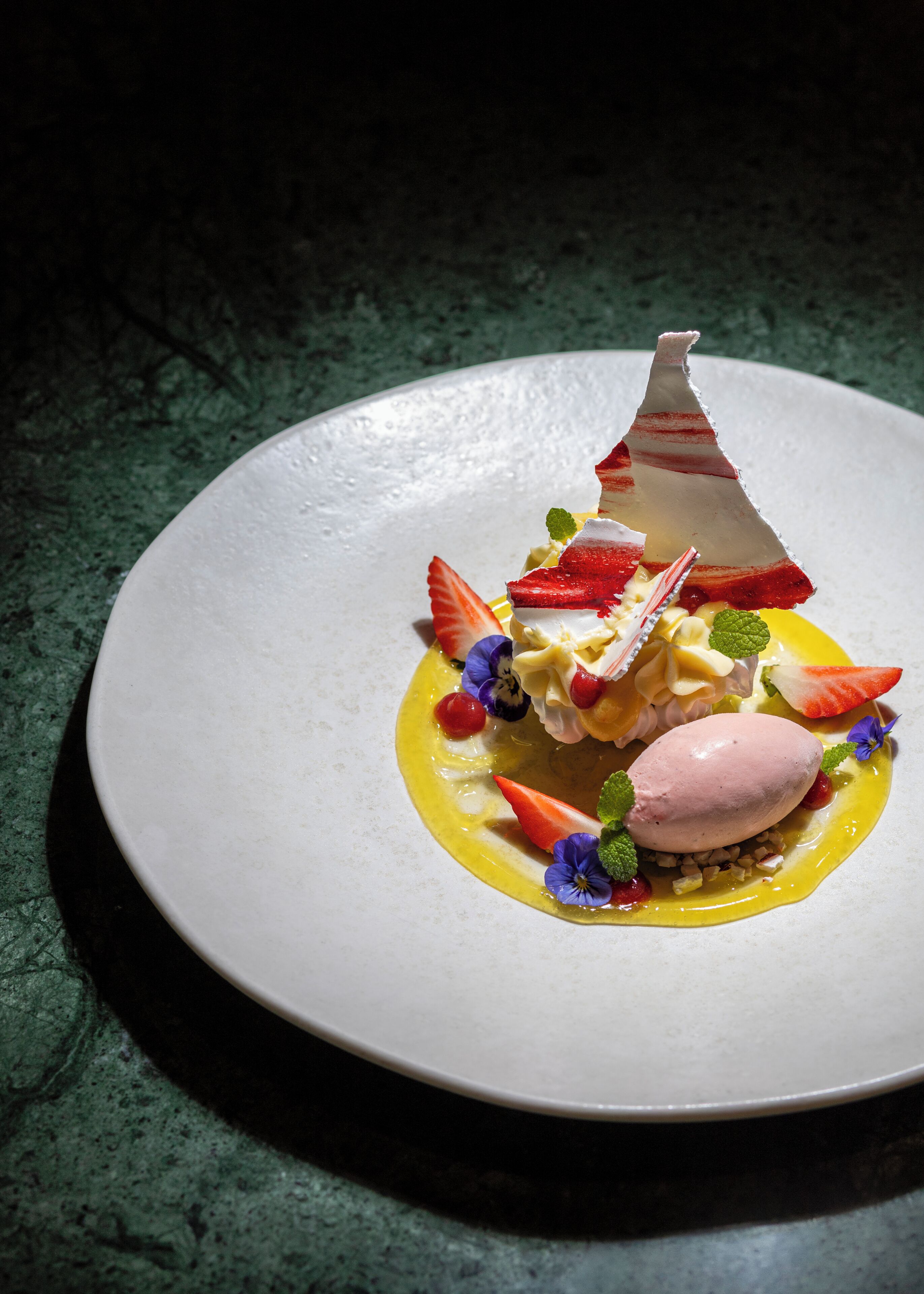A dessert on a white plate with a unique shape, garnished with strawberries and mint leaves.