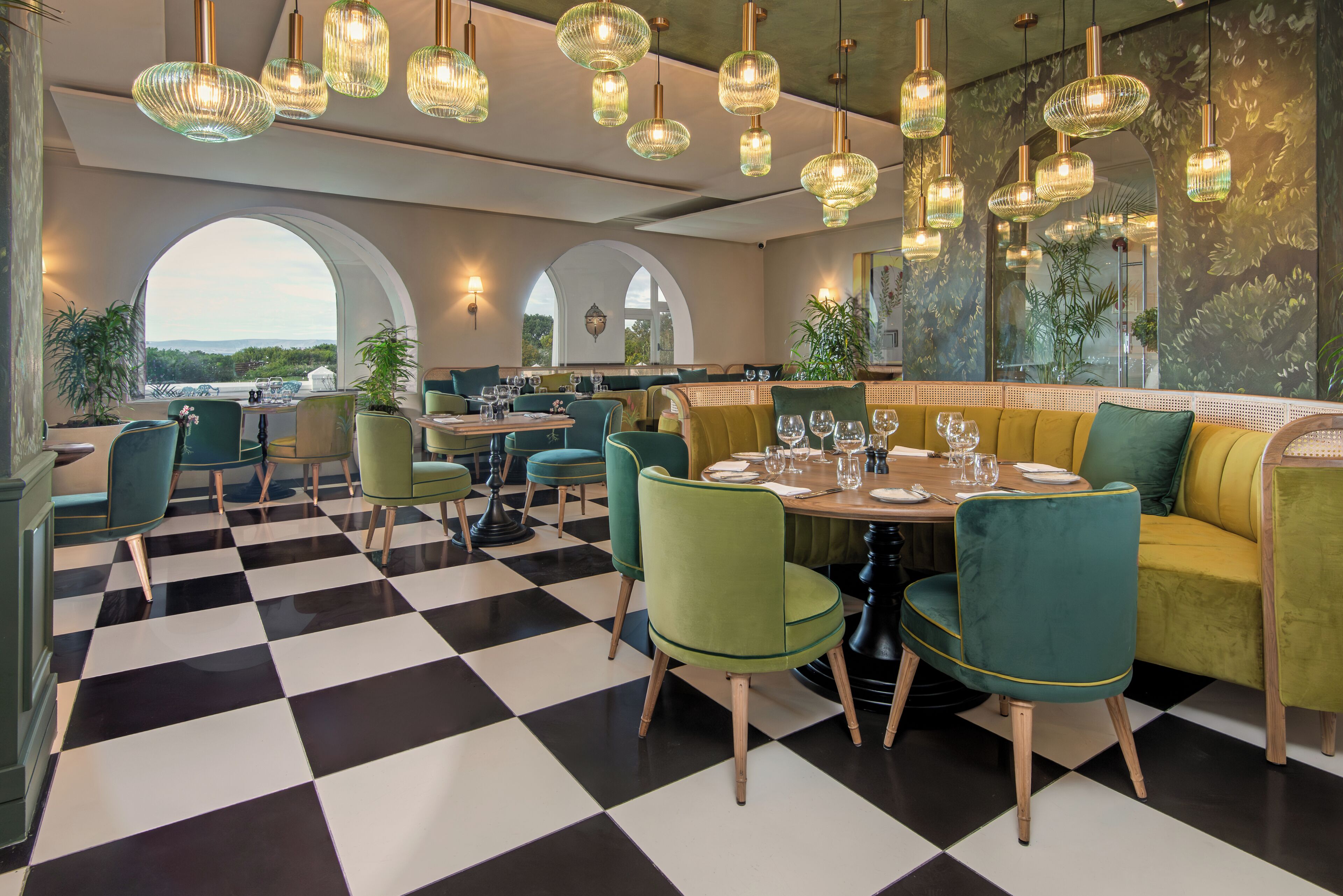 A restaurant with checkered flooring, green and yellow seating, and multiple hanging light fixtures.