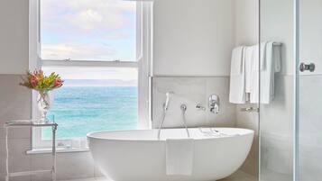 A modern bathroom with a freestanding bathtub, a glass shower enclosure, and a view of the ocean through a large window.