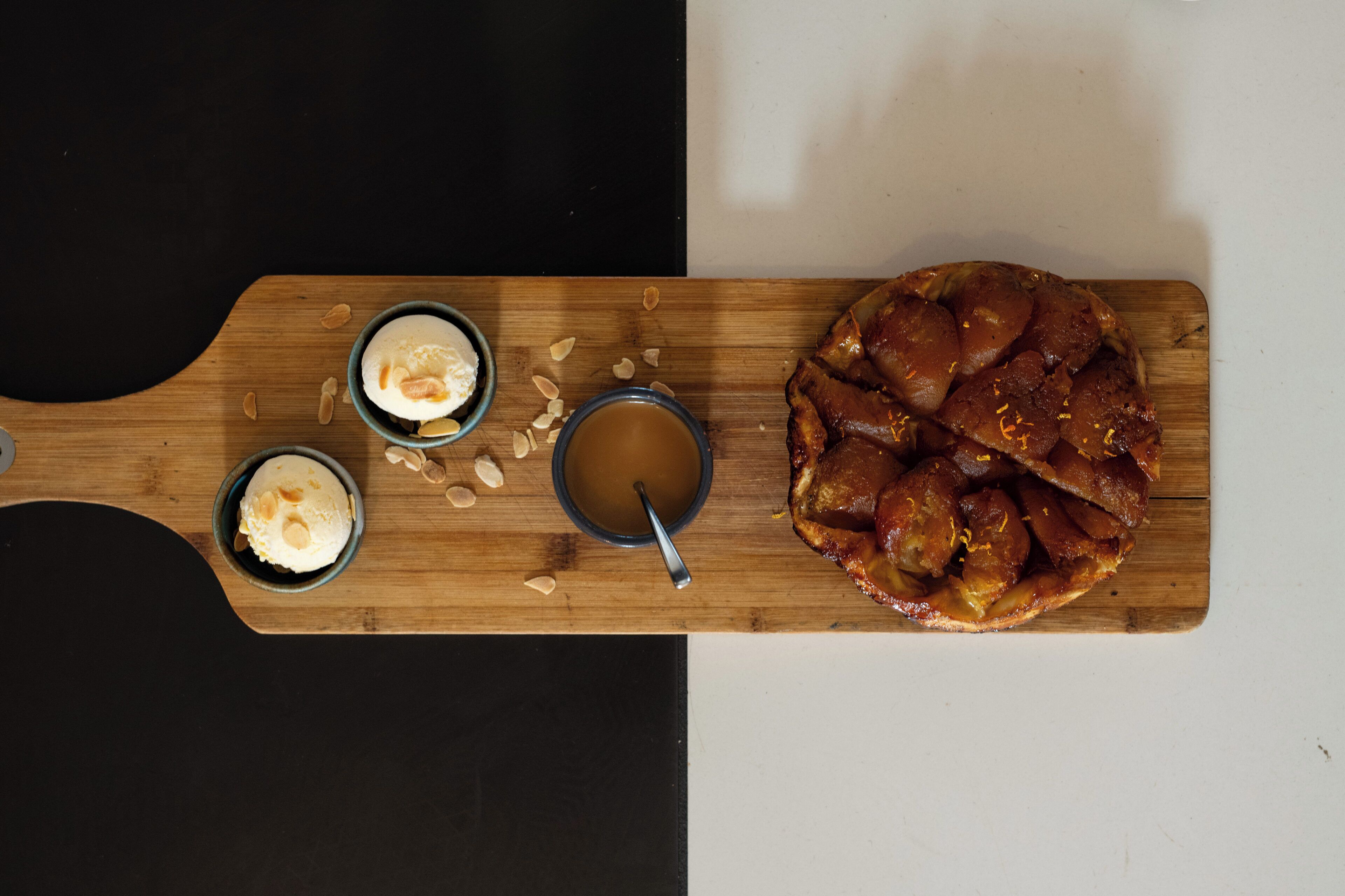 A wooden board with two bowls of ice cream, a cup of coffee, and a pastry.