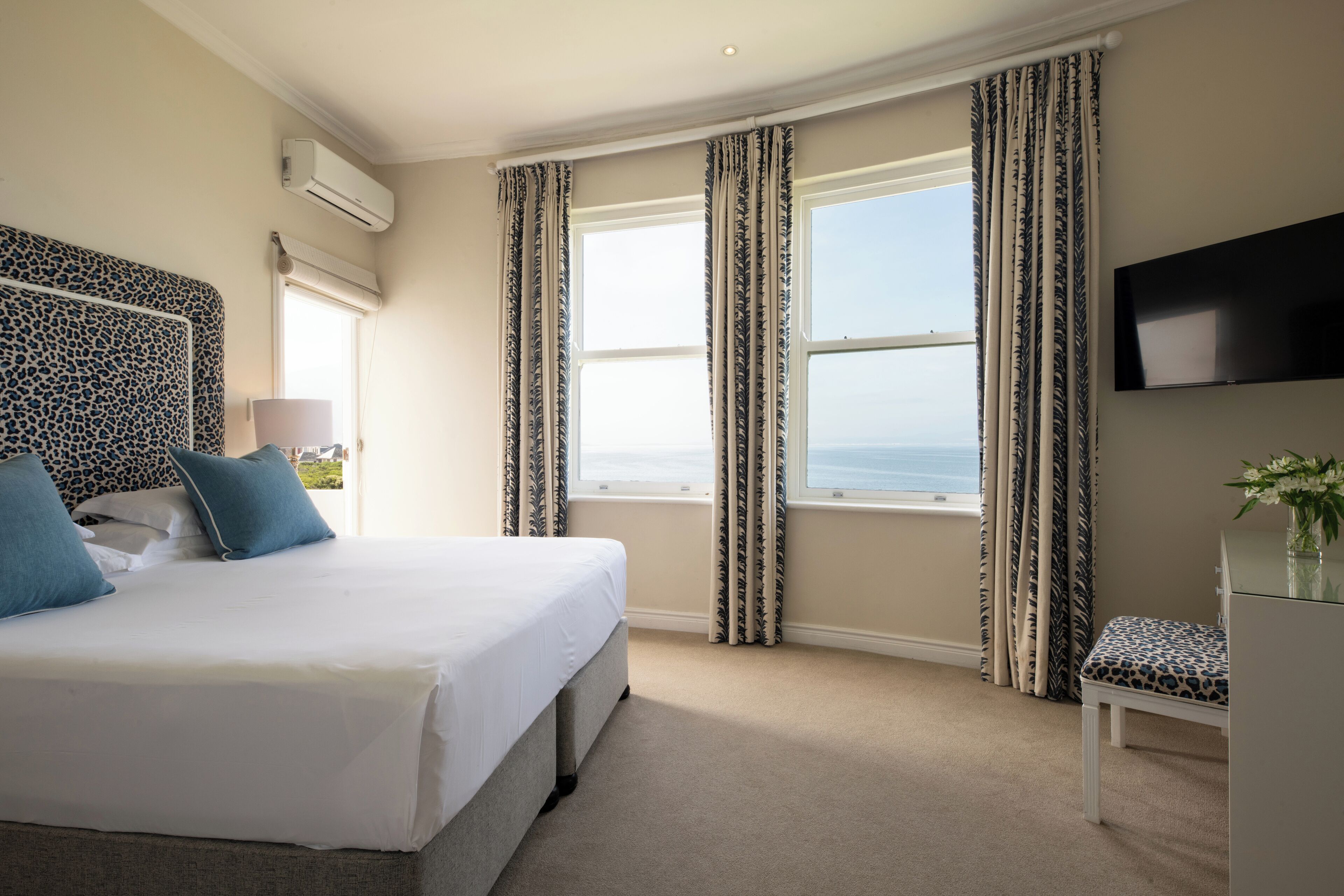 Habitación de hotel con cama, televisión, ventana con cortinas y vista al mar.