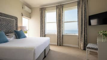 Habitación de hotel con cama, televisión, ventana con cortinas y vista al mar.