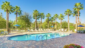 A pool area with lounge chairs and umbrellas, surrounded by palm trees.